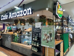 A café named 'Café Amazon' with a sign, a counter with a display of beverages, and hanging plants. - Vanlisut Hotel Ngamwongwan (Nonthaburi)