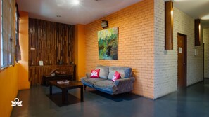 A modern lobby with a wooden accent wall, a sofa with red cushions, and a painting of a forest scene.