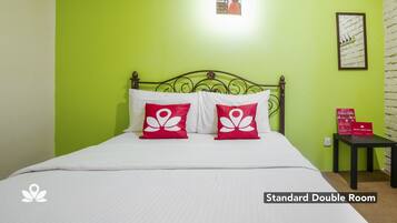 A standard double room with a bed, two red pillows, a nightstand, a framed picture, and a sign on the wall.