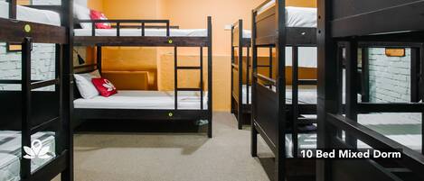 Dormitorio mixto para 10 personas, con literas, pared de ladrillo, unidad de aire acondicionado y piso alfombrado.