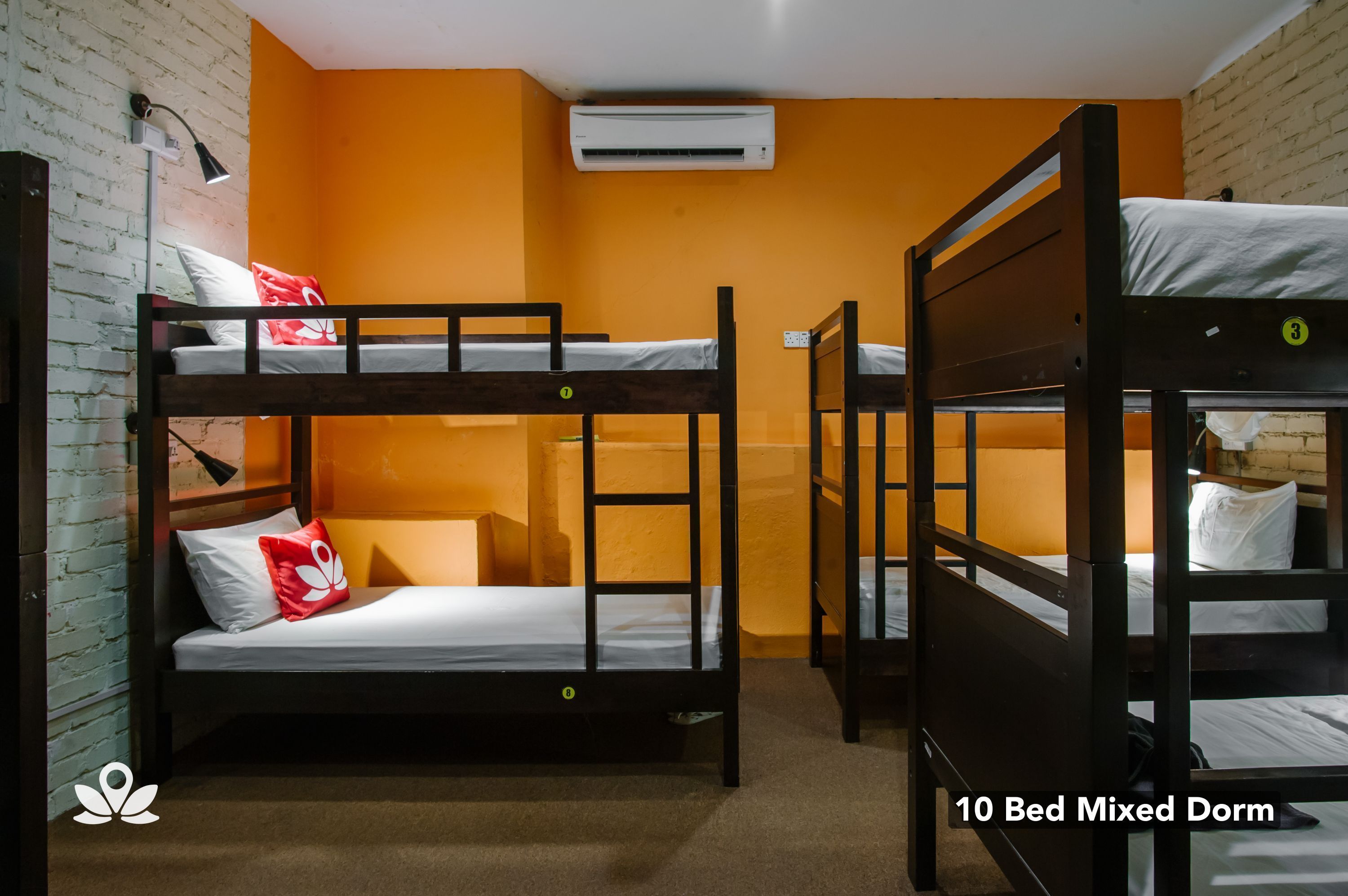 Un dormitorio mixto para 10 personas con literas, una pared de ladrillo, un equipo de aire acondicionado y una lámpara.