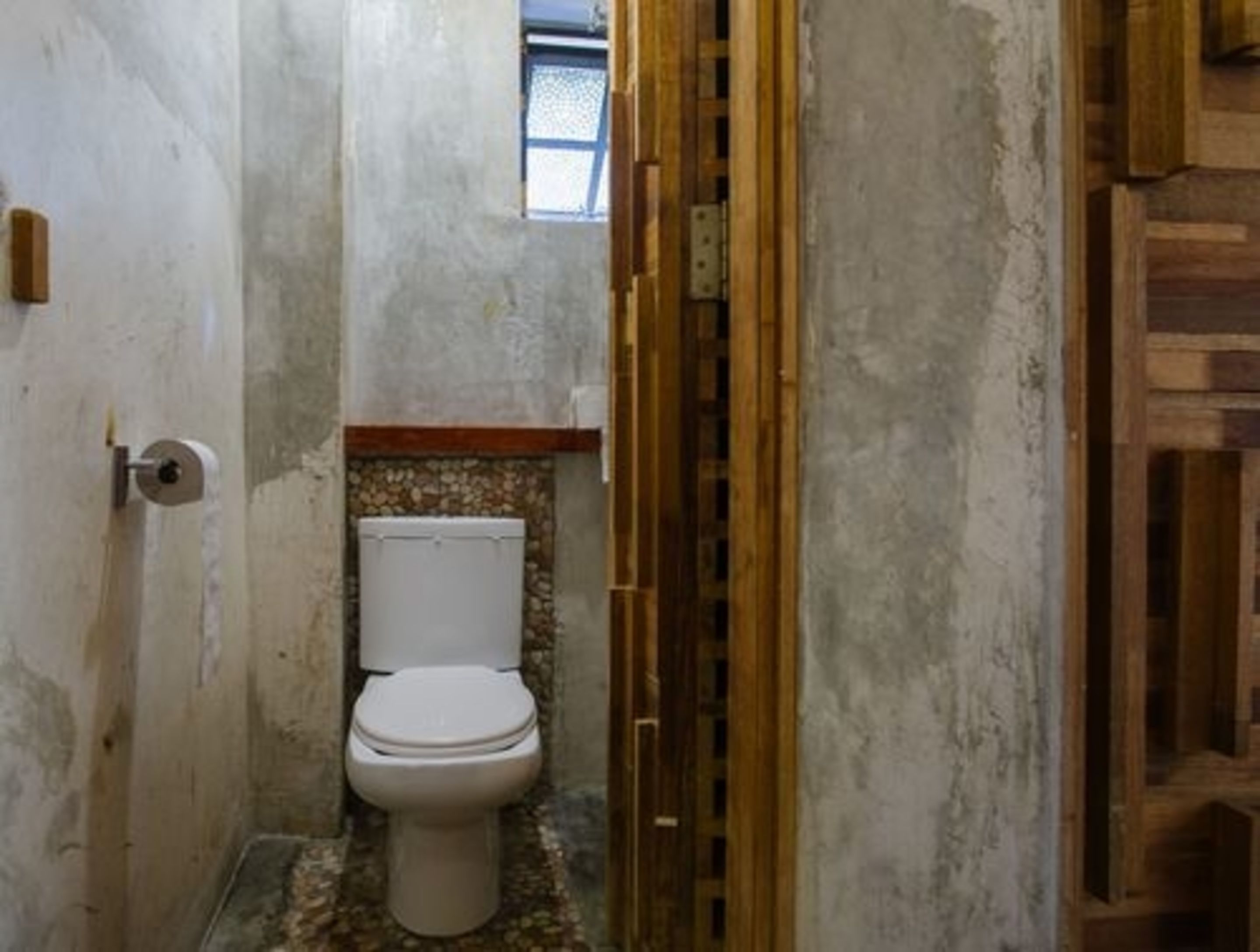 Un baño pequeño y estrecho con un inodoro, una puerta de madera y una ventana.