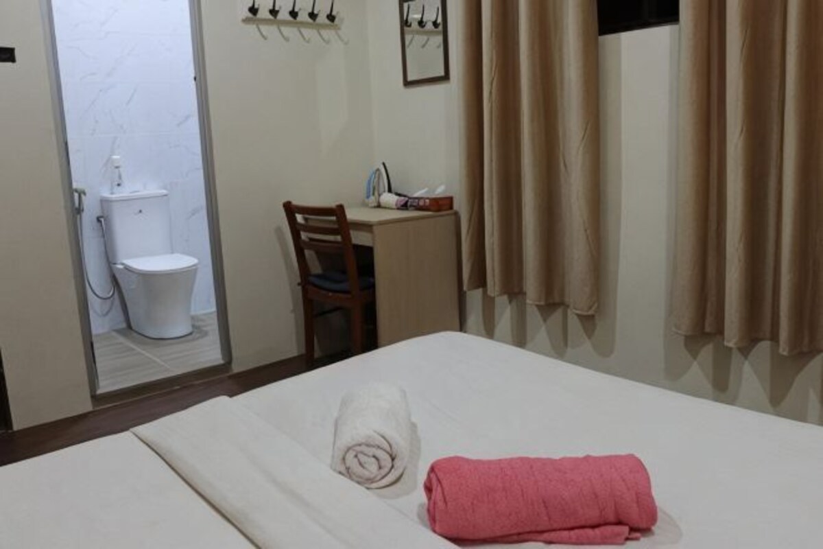A hotel room with a bed, a chair, a desk, a toilet, and a mirror.