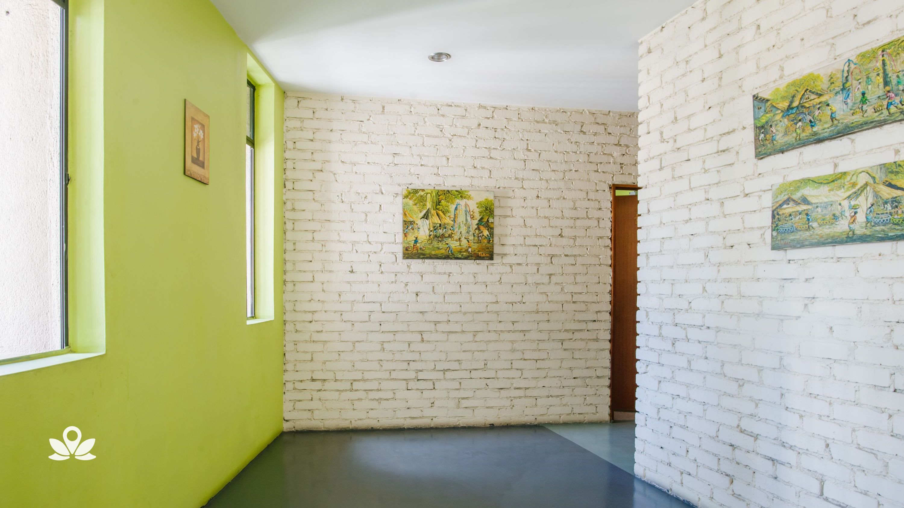 Corredor com paredes de tijolo branco, paredes verdes em um lado e uma porta no final. Há três quadros na parede.