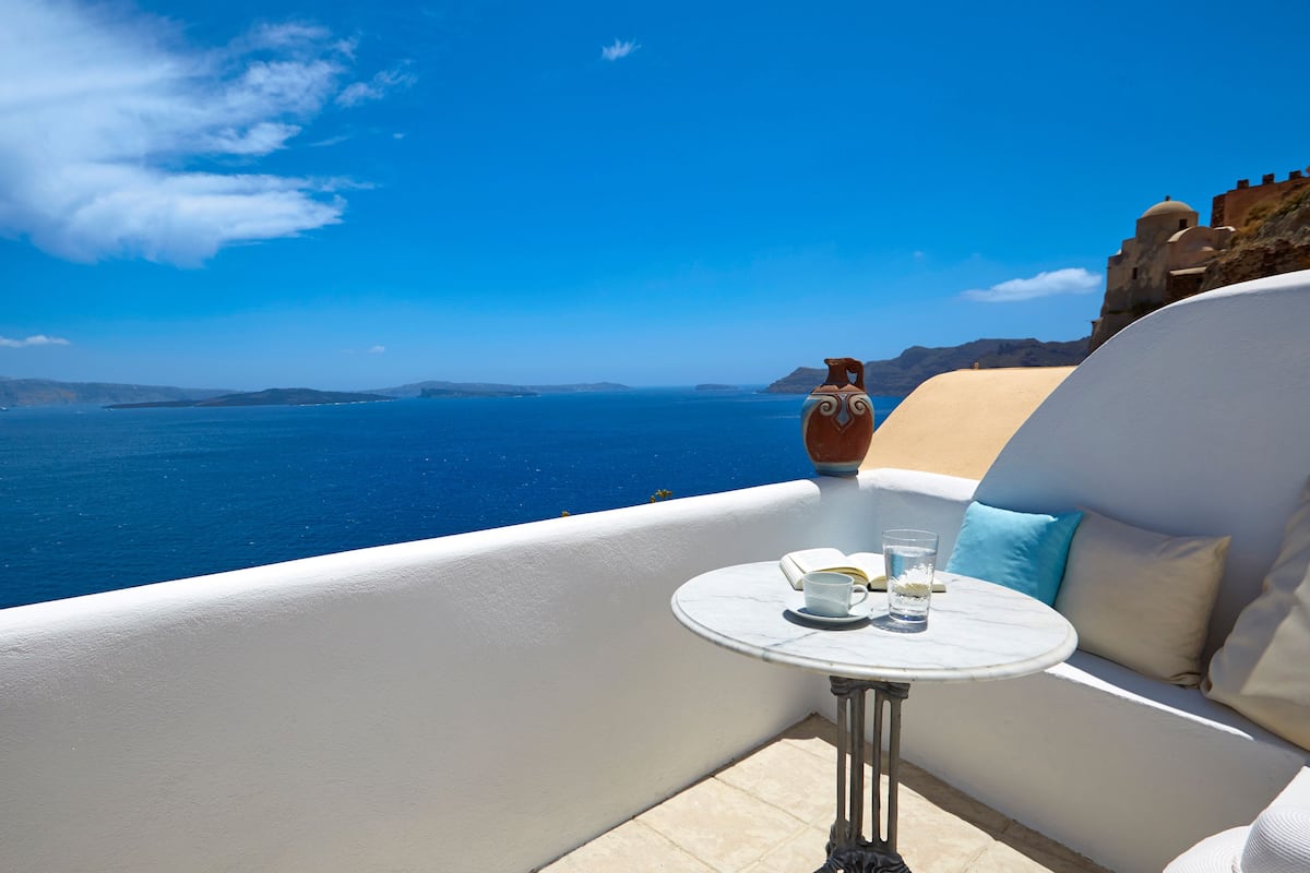 A balcony with a white table, a vase, and a view of the sea and distant islands.