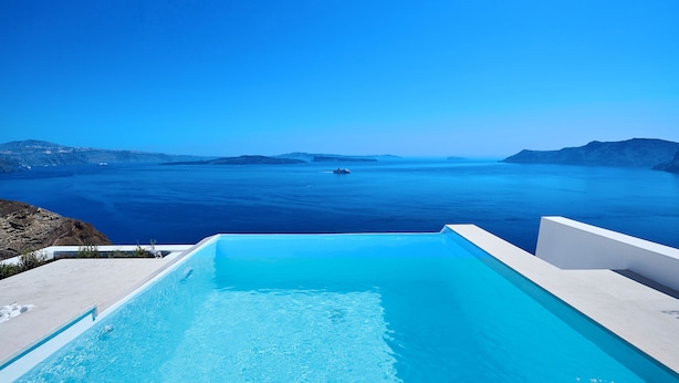 Cielo azul despejado, piscina y vista al mar con un barco a lo lejos.