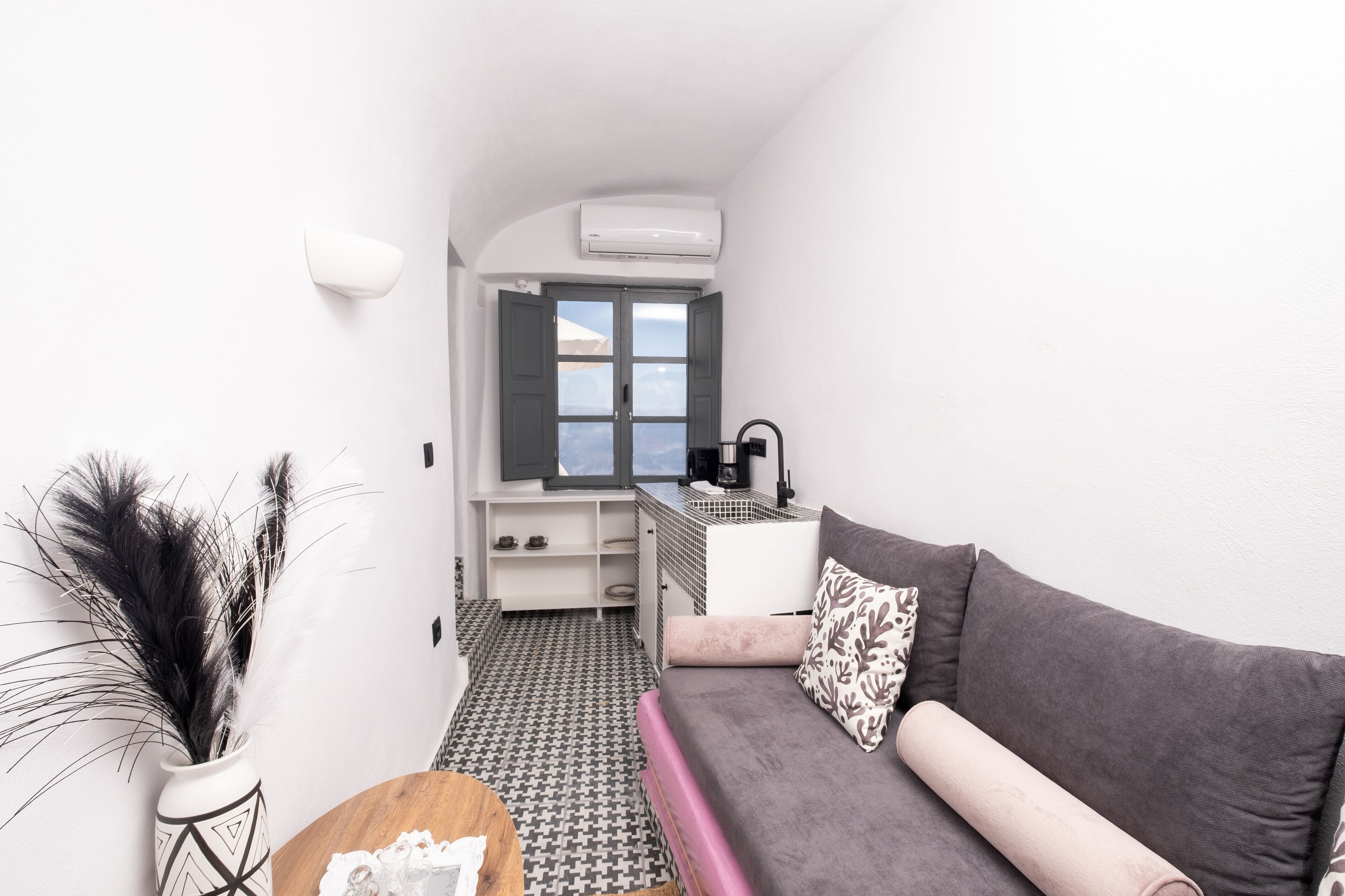 Un espacio habitable compacto con kitchenette, un sofá con cojines estampados, un florero decorativo con plumas y un piso con diseño.