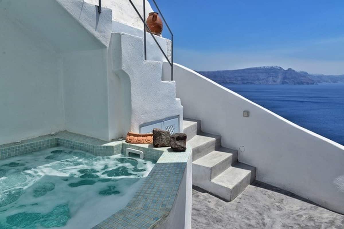 A hot tub with a view of the sea, white walls, and a stone pathway leading to a door.