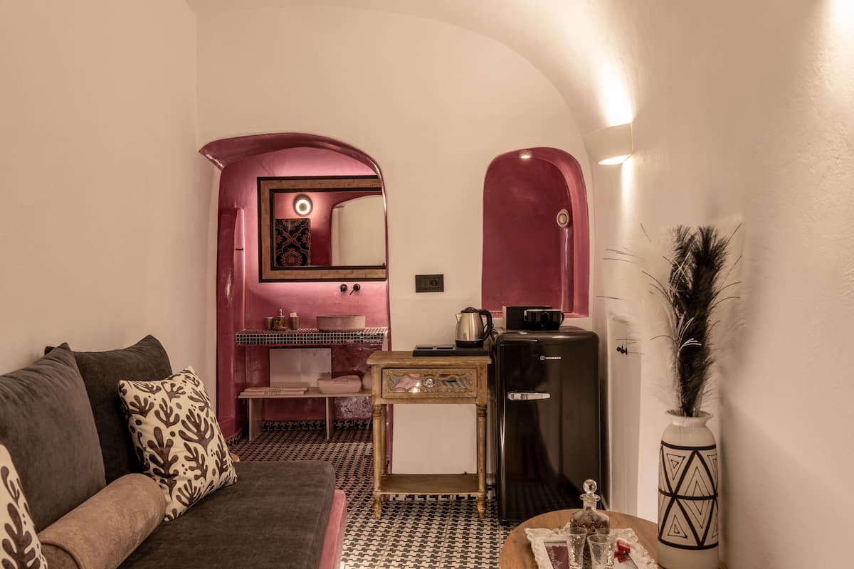 A compact living space with a sofa, a small table, a refrigerator, and a decorative vase.
