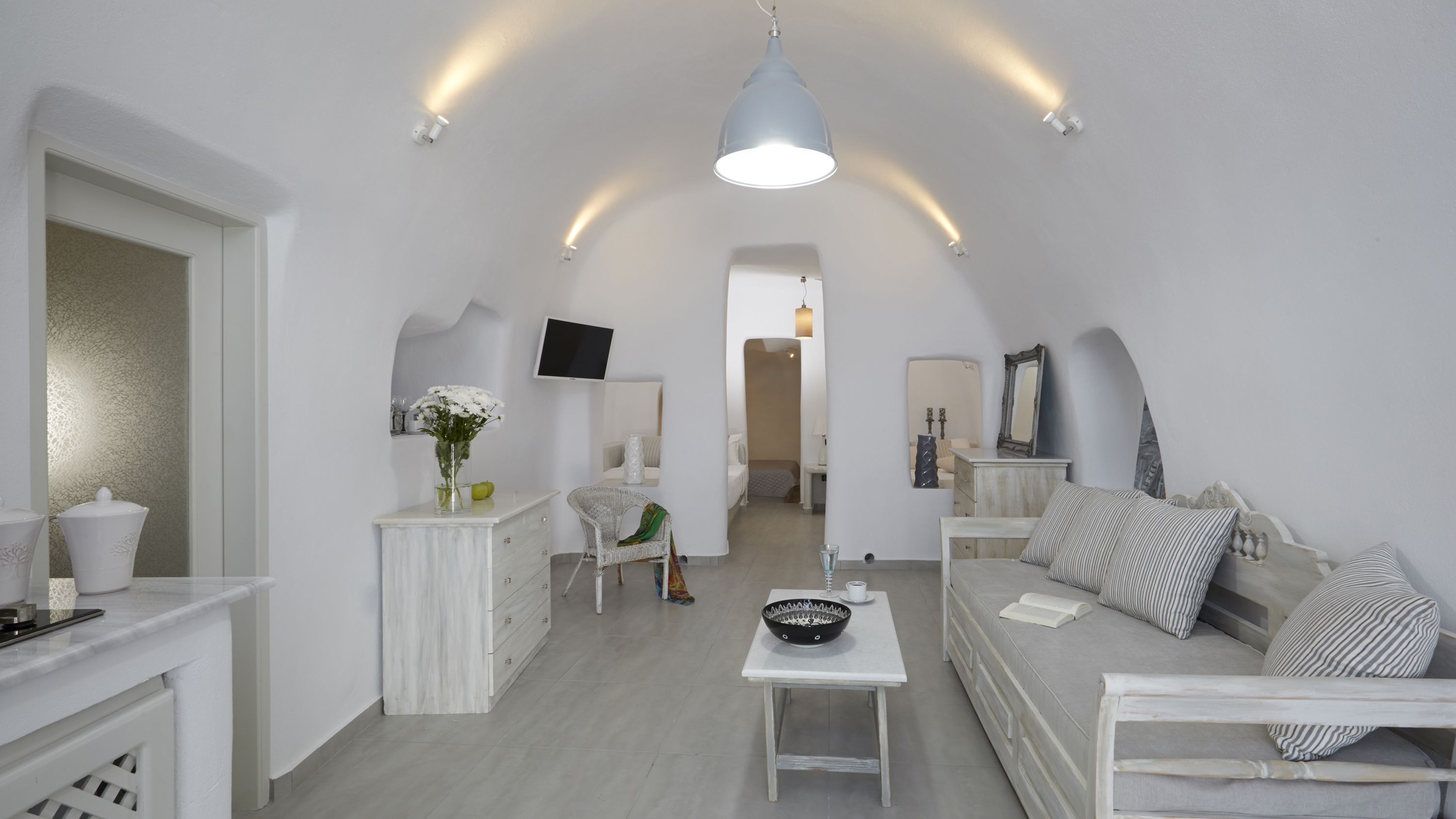 A spacious loft bedroom with a high ceiling, a large bed, a seating area with a sofa, a small table, and a television mounted on the wall.