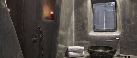 A modern bathroom with a large, round vessel sink, a handheld showerhead, and a small window.