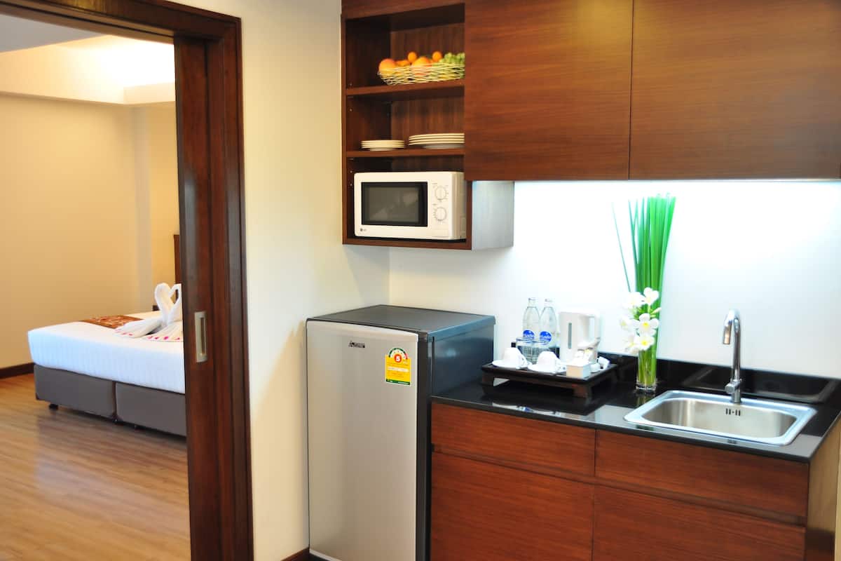 A compact kitchen with a microwave, sink, and a small refrigerator. There is a bed in the adjacent room.