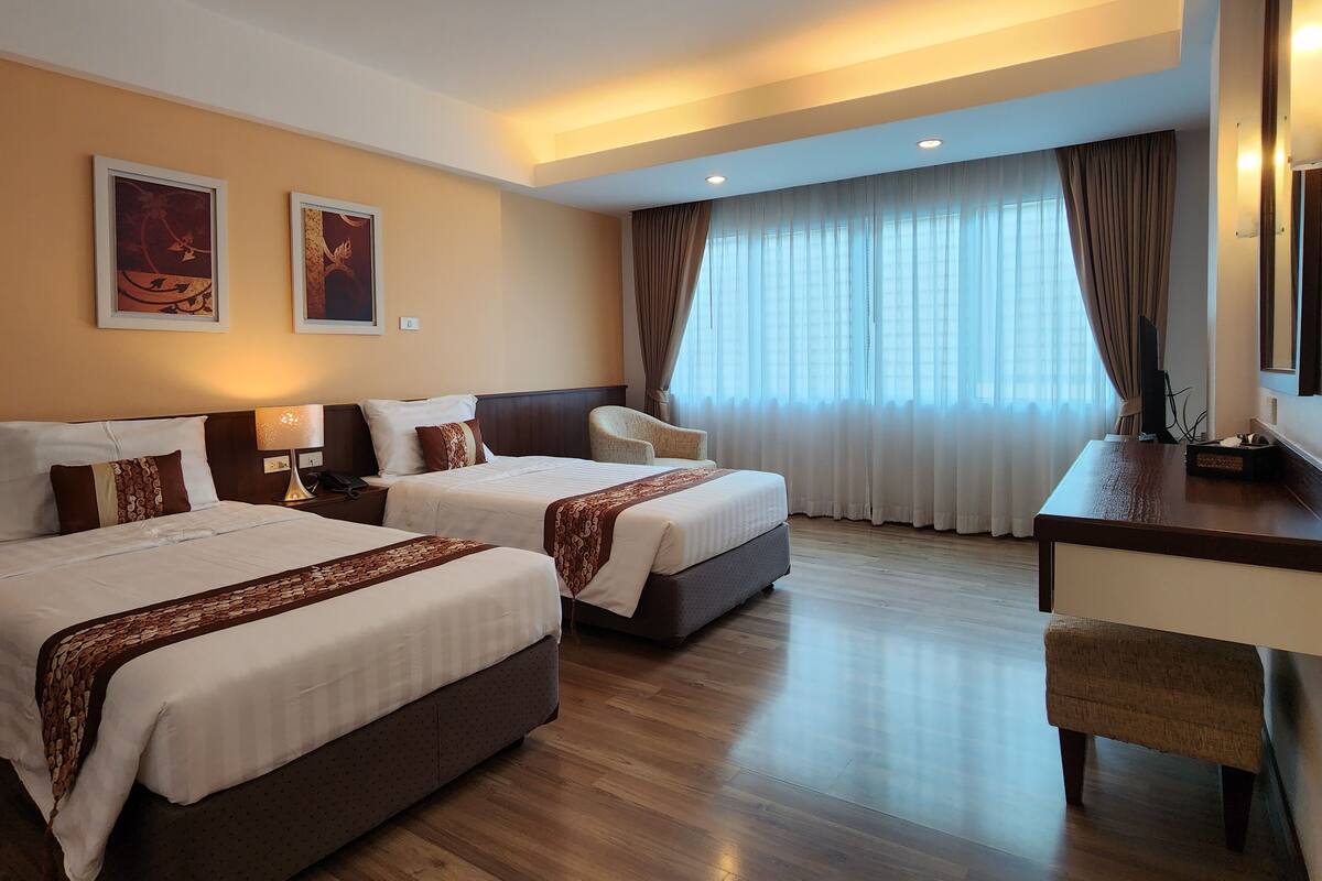 A hotel room with two beds, a desk, a chair, and a large window with curtains.