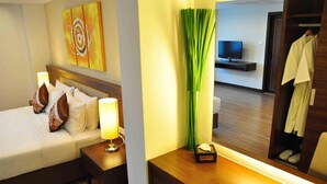 A hotel room with a bed, bedside table, lamp, artwork, a mirror, and a television in the background. - Avion Hotel (Bangkok)