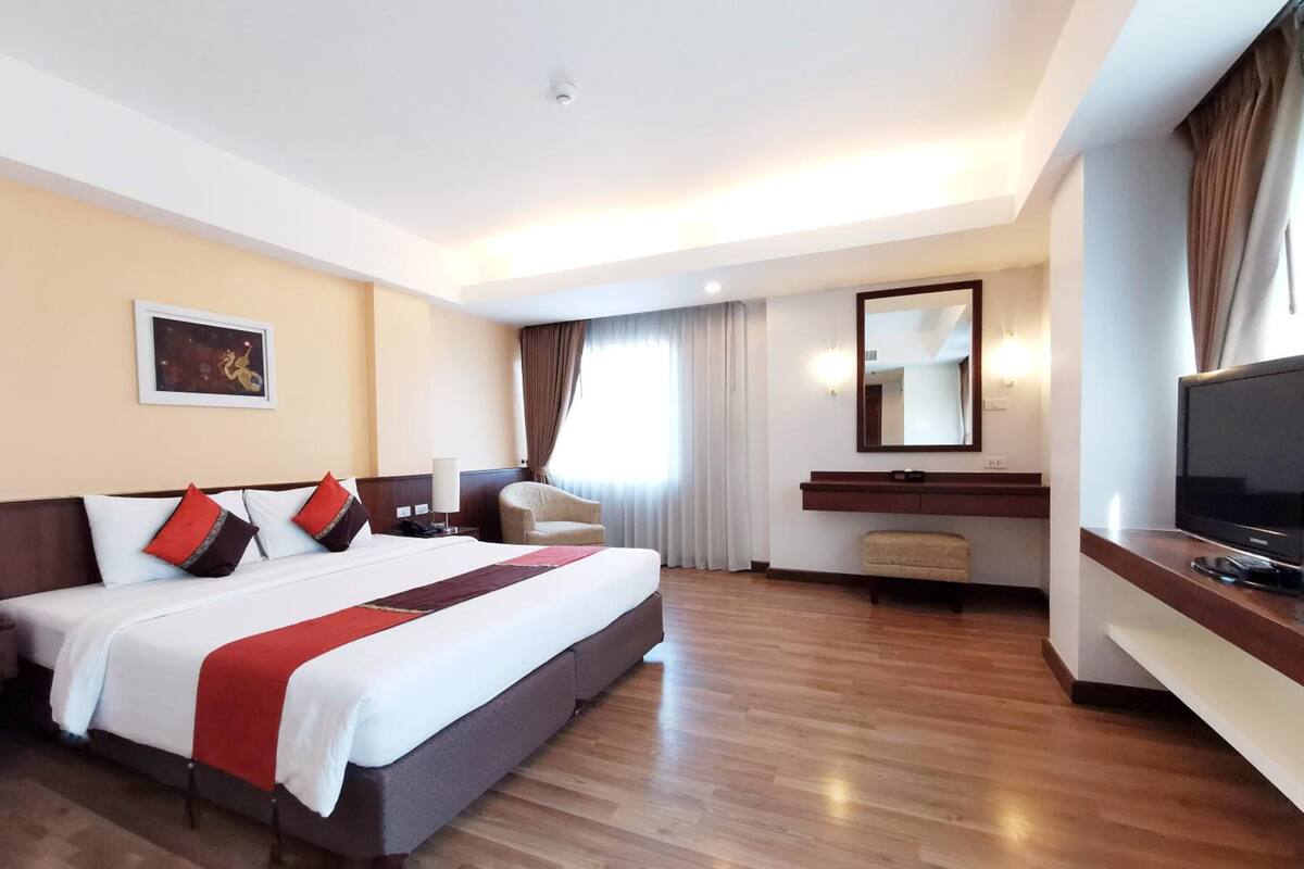 A hotel room with a large bed, a TV, a desk, and a chair.