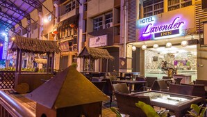 An outdoor seating area with wicker furniture and a thatched-roof structure, a sign for Hotel Lavender Inn, and a visible storefront for Saturn Ham Beauty. - Lavender Inn Permas Jaya (Masai)