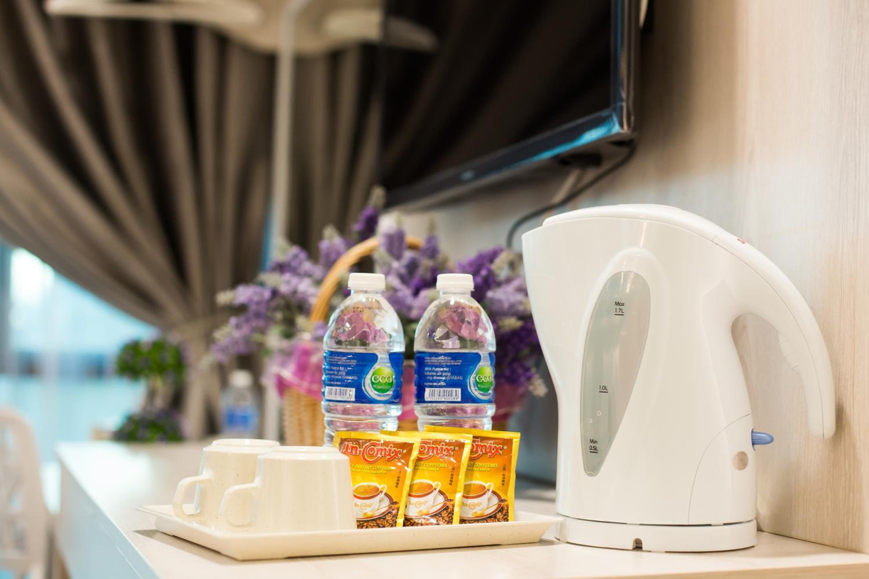 A countertop with a white electric kettle, two water bottles, and three packets of instant coffee.