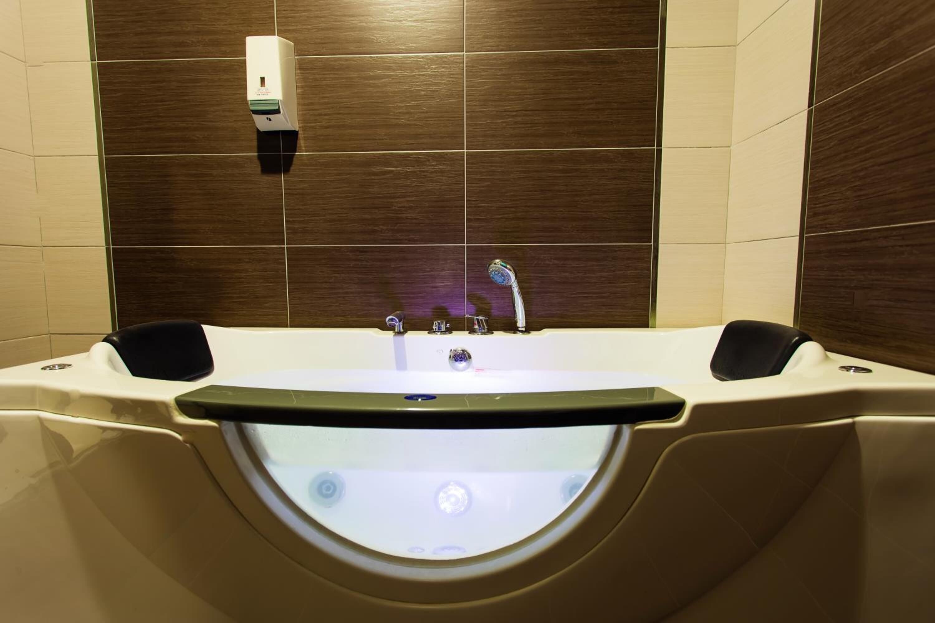 Une salle de bain moderne avec une grande baignoire, une douchette à main et un distributeur de savon fixé au mur.