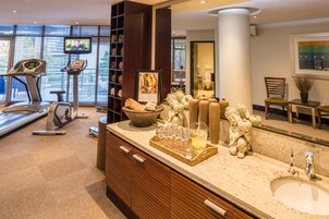 A modern bathroom with a large mirror, a sink, and a vanity. There is a treadmill in the adjacent room.