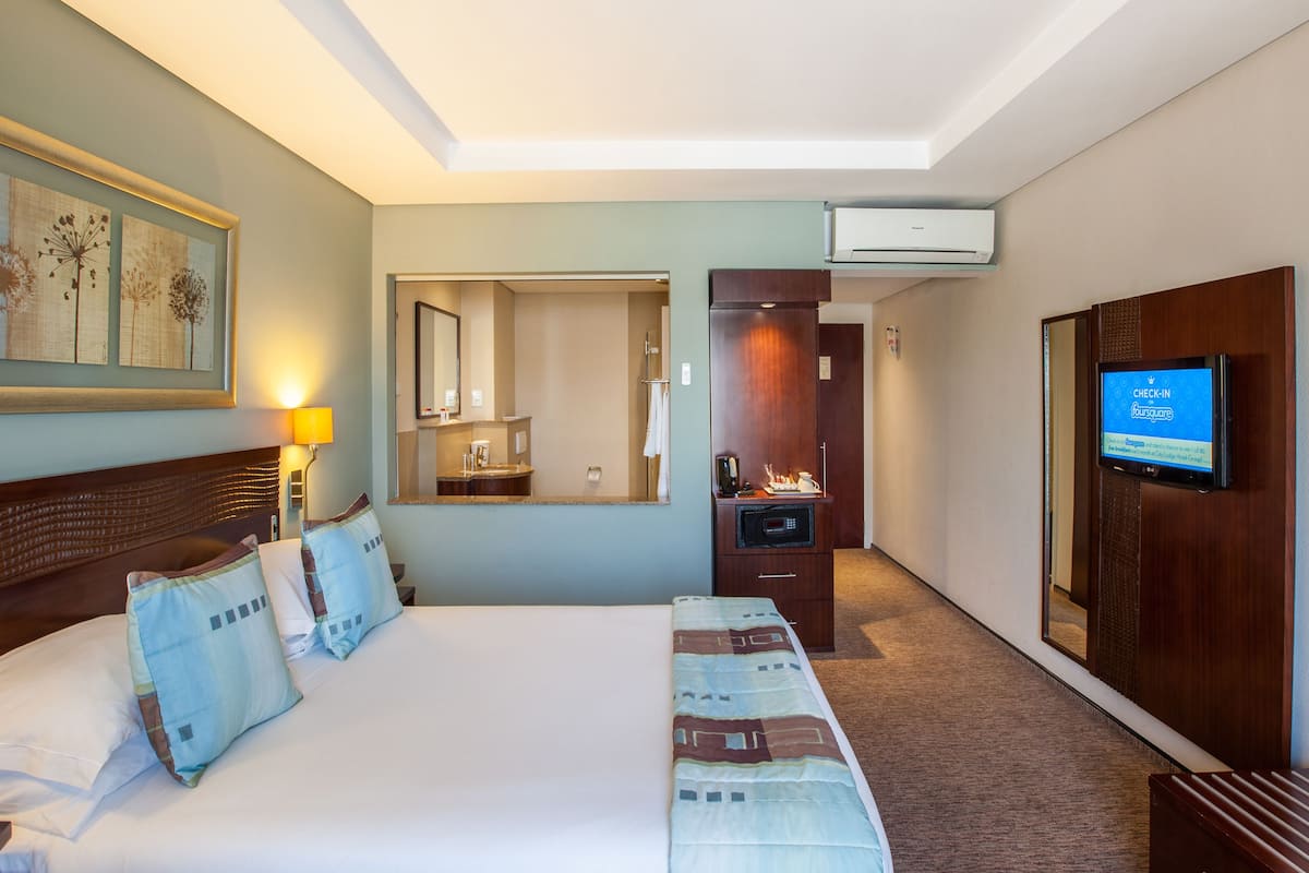 A hotel room with a large bed, a bathroom with a mirror and sink, a television, and a carpeted floor.