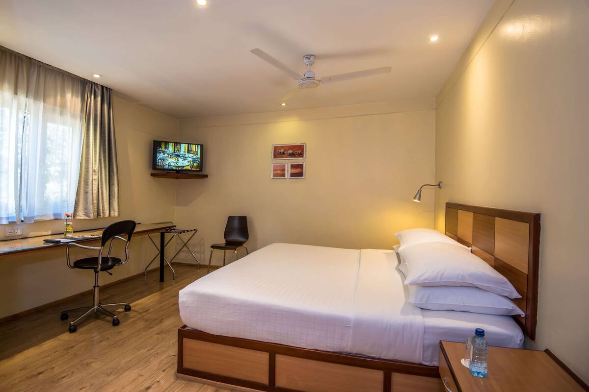 Een hotelkamer met een bed, bureau, stoel, televisie en plafondventilator.