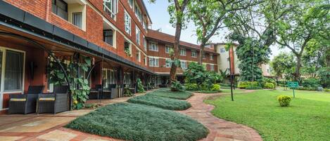 A brick building with a courtyard featuring a stone pathway, green hedges, and outdoor seating.