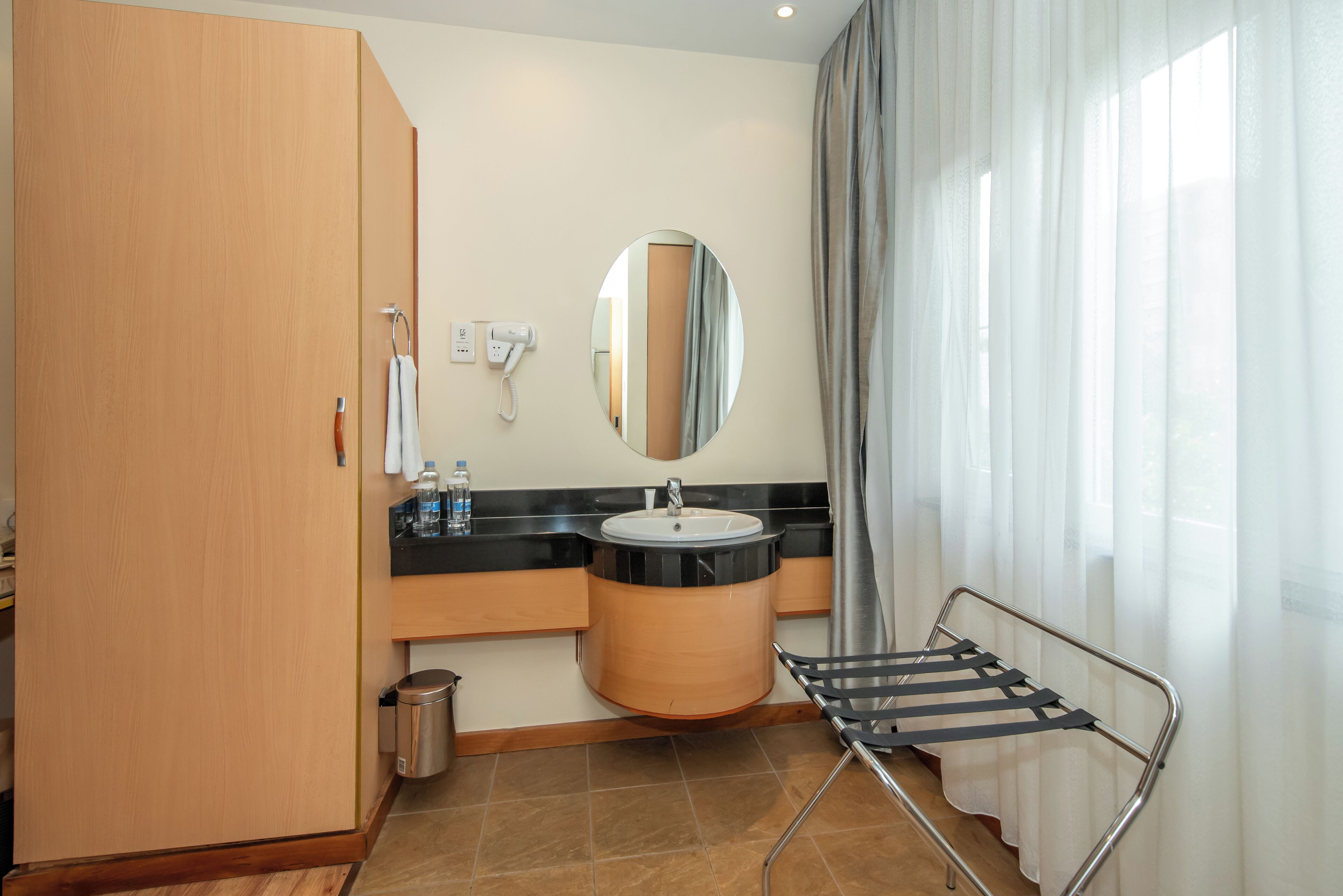 A bathroom with a wooden wardrobe, a sink with a mirror, a towel rack, and a window with curtains.