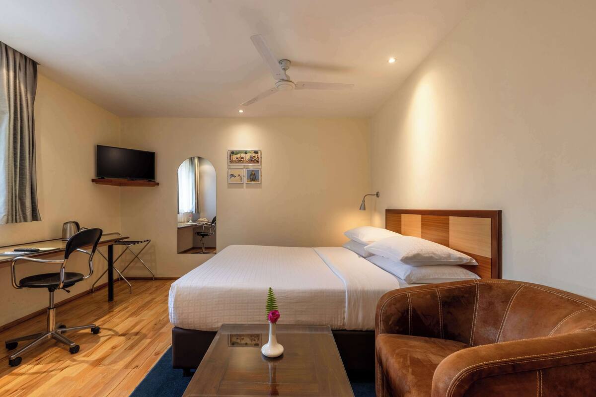Een hotelkamer met een bed, een bureau, een stoel, een televisie en een plafondventilator.