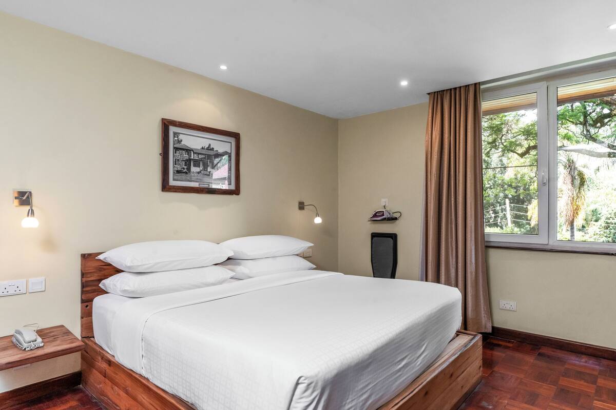 Een keurig opgemaakt bed met witte lakens in een kamer met houten vloeren, een ingelijst schilderij aan de muur, en een raam met gordijnen.