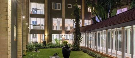 Un patio con césped cuidado, mobiliario exterior y un edificio con ventanas grandes y un letrero visible.