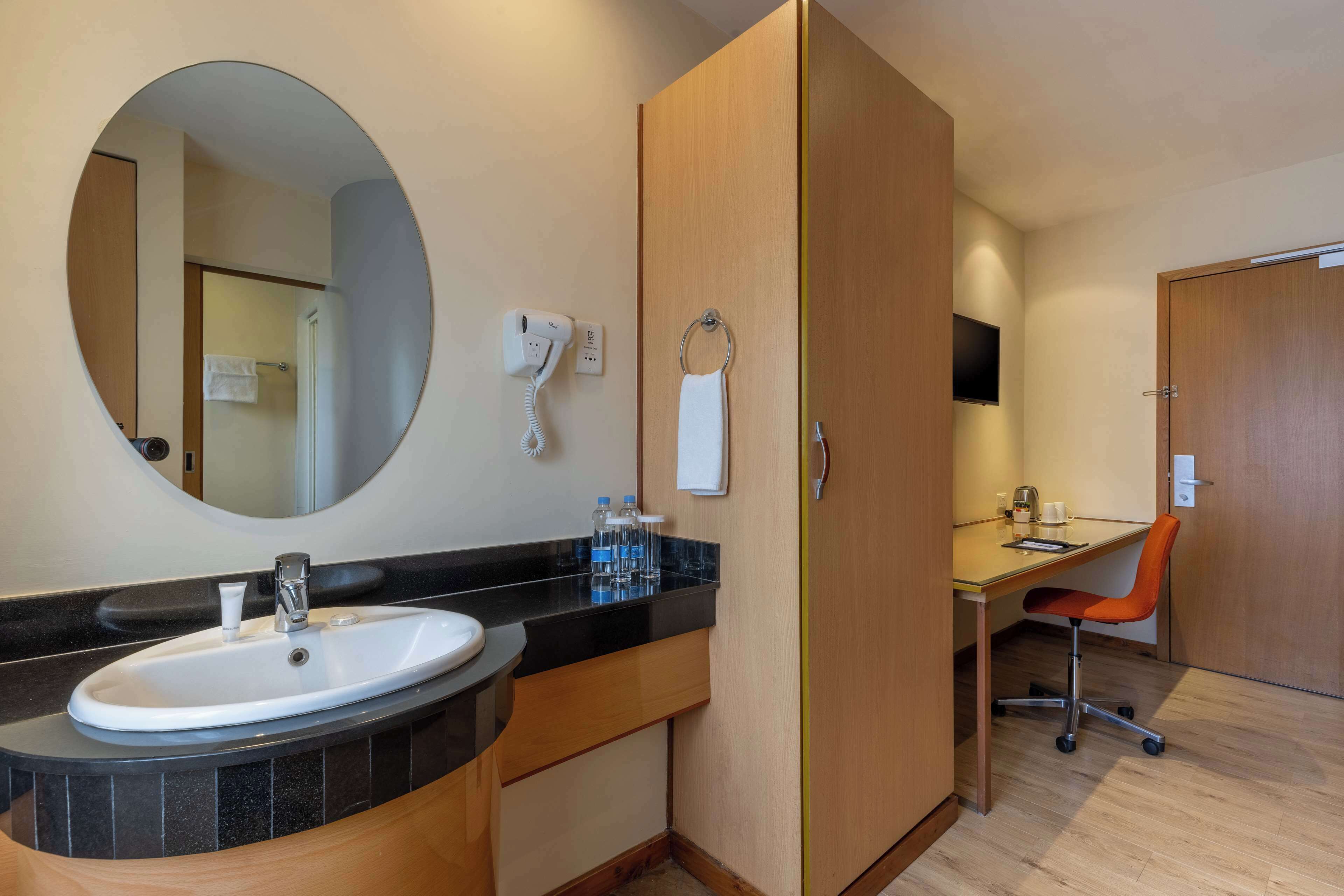 A bathroom with a round mirror, a sink, a hairdryer, and a towel ring.