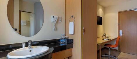 Un baño con un espejo redondo, un lavabo, un secador de pelo y un aro para toallas.