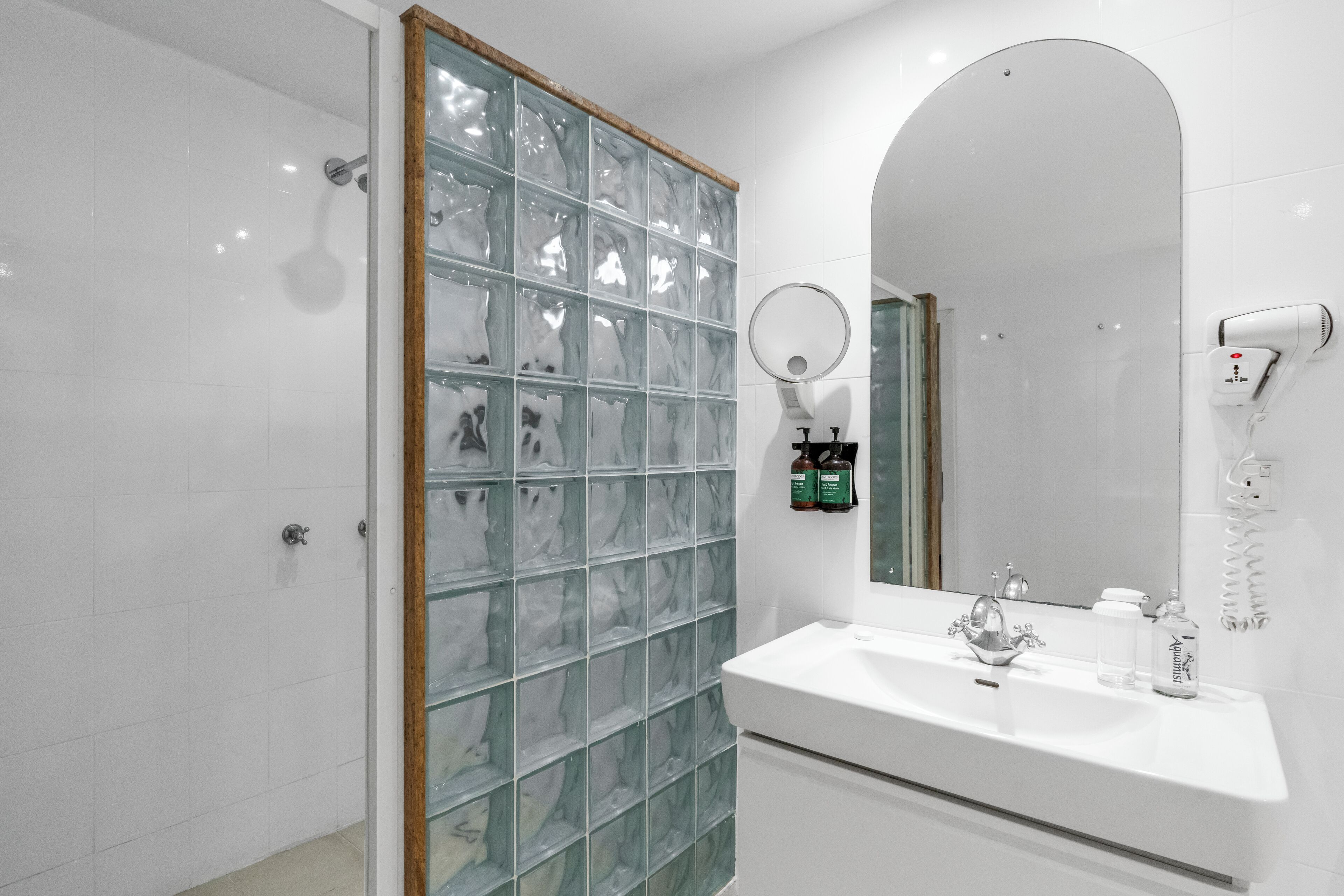 Une salle de bain avec une douche à parois de verre, un lavabo avec un miroir et un sèche-cheveux fixé au mur.