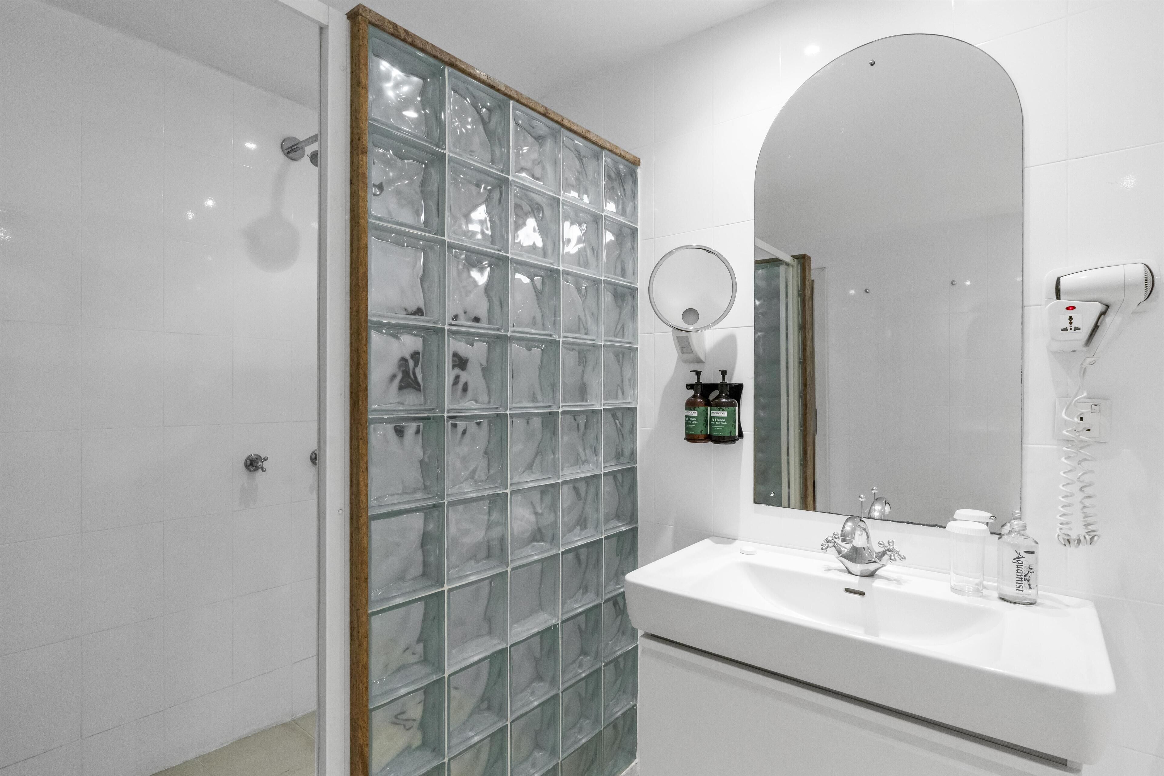 Une salle de bain avec une douche à parois de verre, un lavabo avec un miroir et un sèche-cheveux fixé au mur.