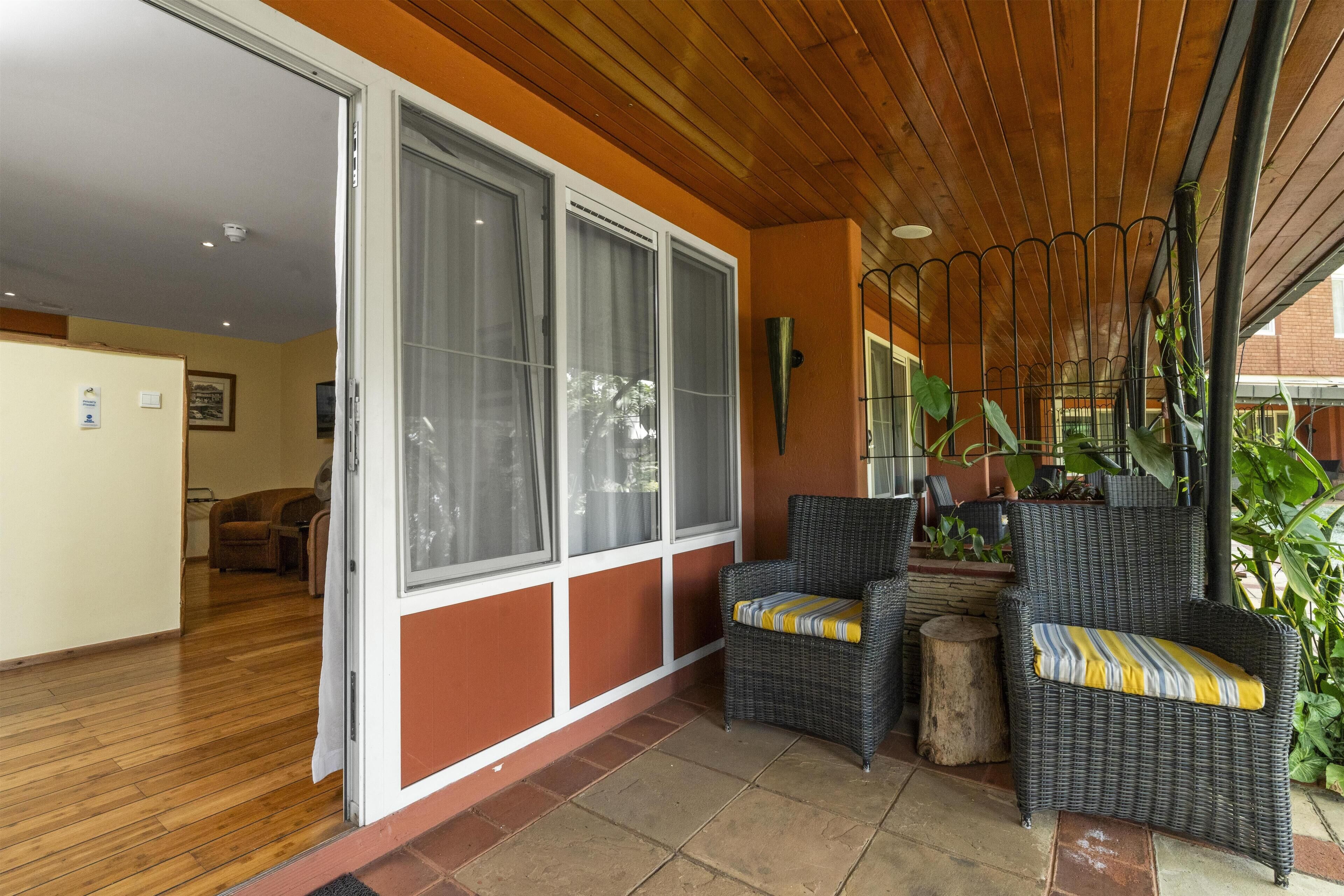 Una habitación con puerta corrediza de vidrio que da a un patio con sillas de mimbre y plantas en macetas.