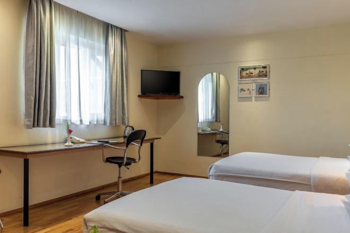 Een hotelkamer met twee bedden, een bureau met stoel, een televisie en een spiegel.