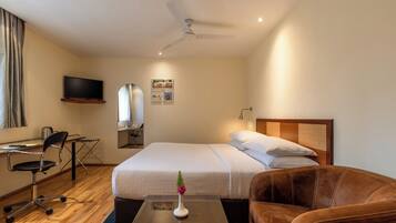 Habitación de hotel con cama, escritorio, silla, televisión y ventilador de techo.