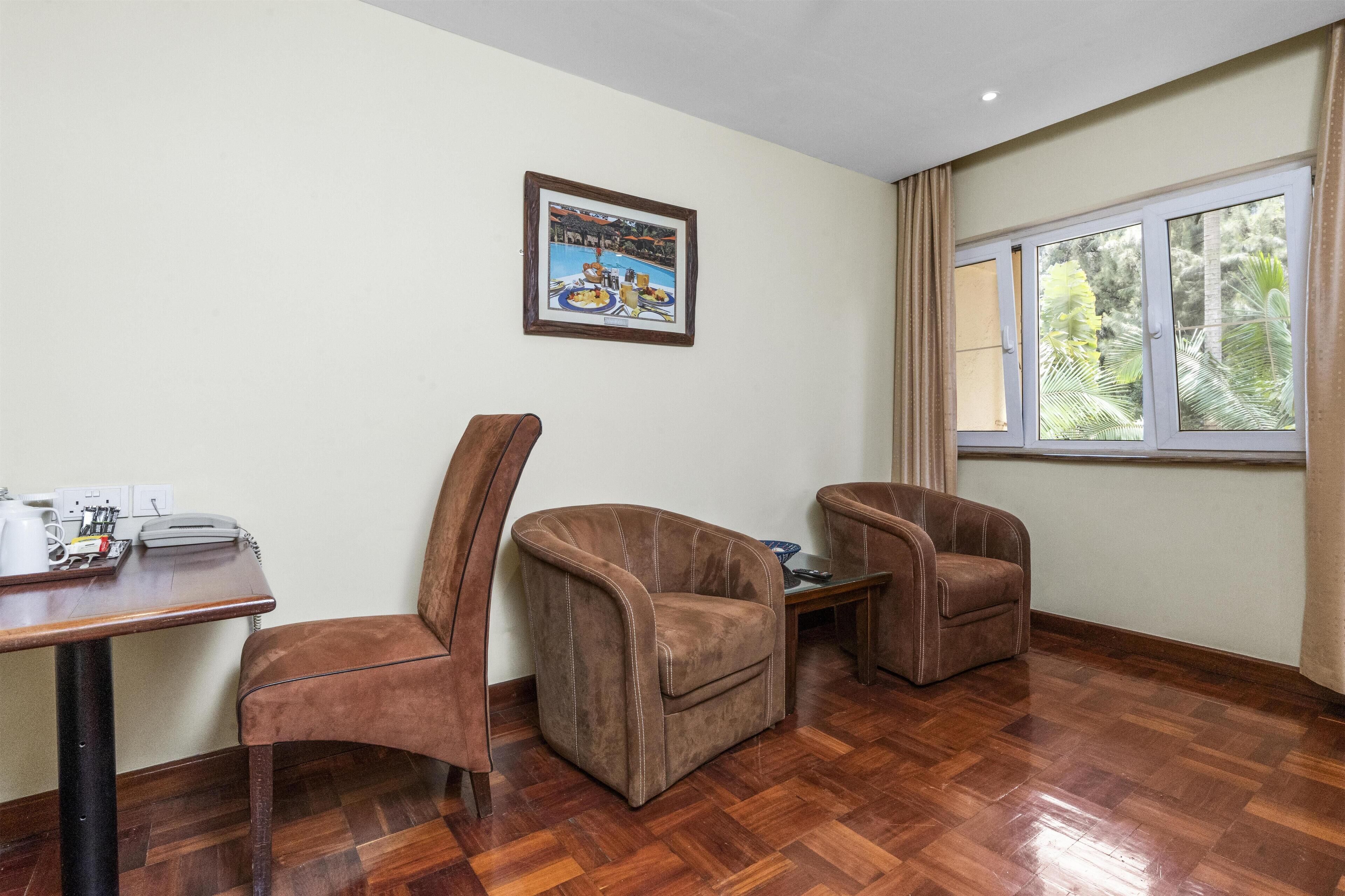 A room with two brown leather chairs, a wooden table with a telephone, and a framed picture on the wall.