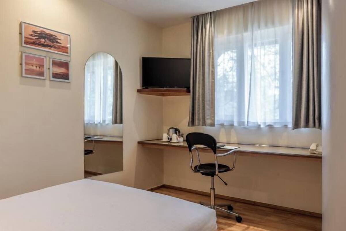 Habitación de hotel con cama, escritorio con silla, televisor sobre el escritorio y ventana con cortinas.