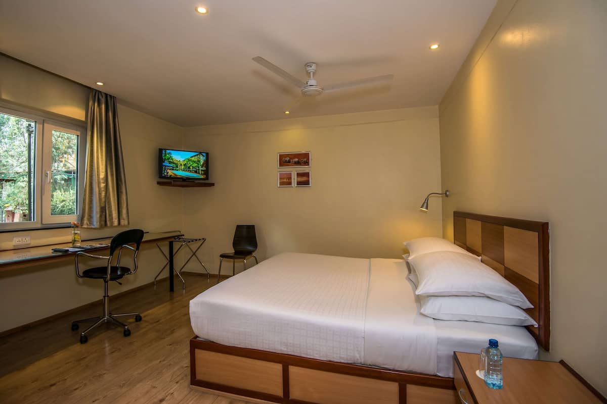 Een hotelkamer met een bed, bureau, stoel, televisie en een raam met gordijnen.