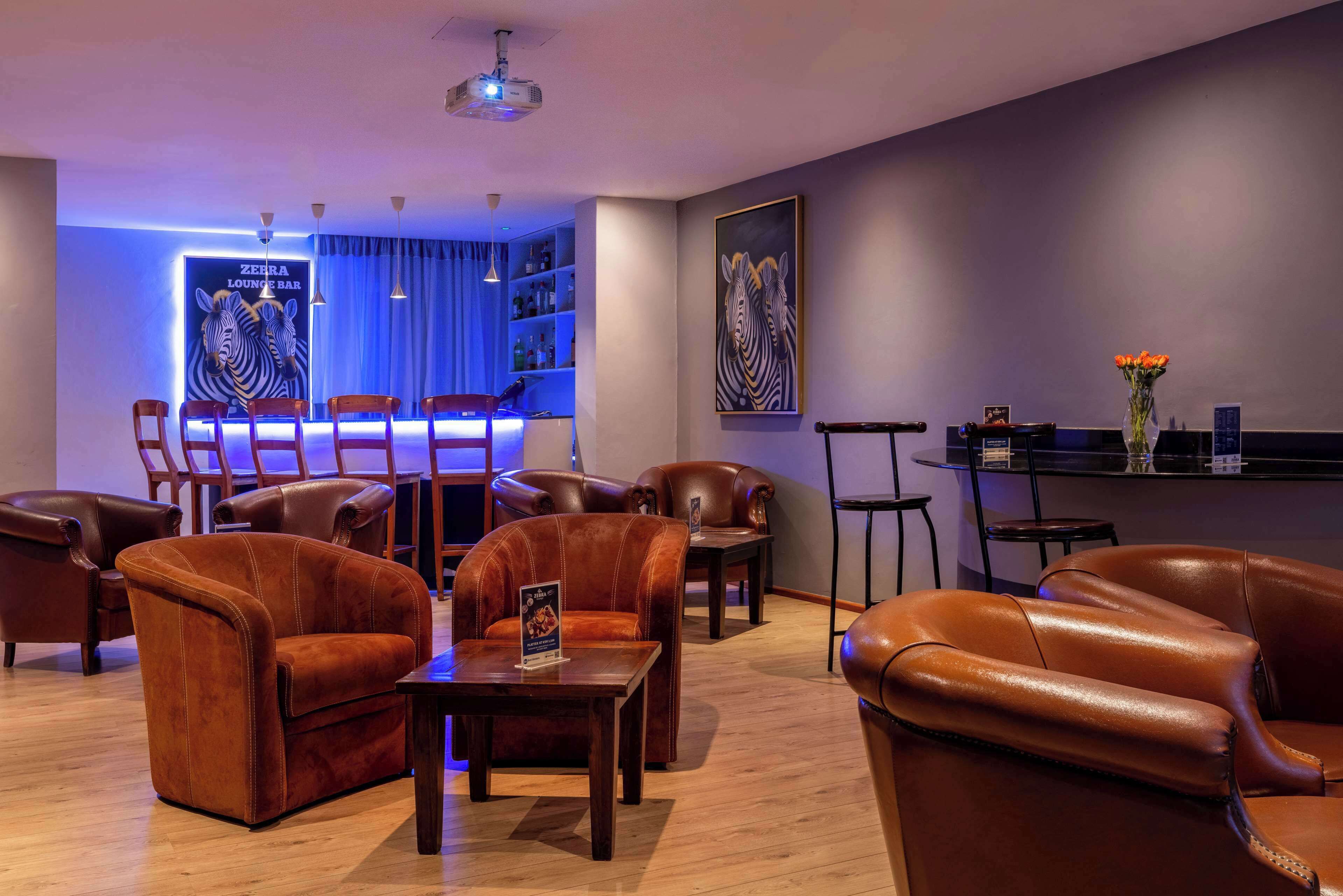 Zona relax con divani in pelle, angolo bar illuminato di blu e un'opera d'arte a tema zebra.