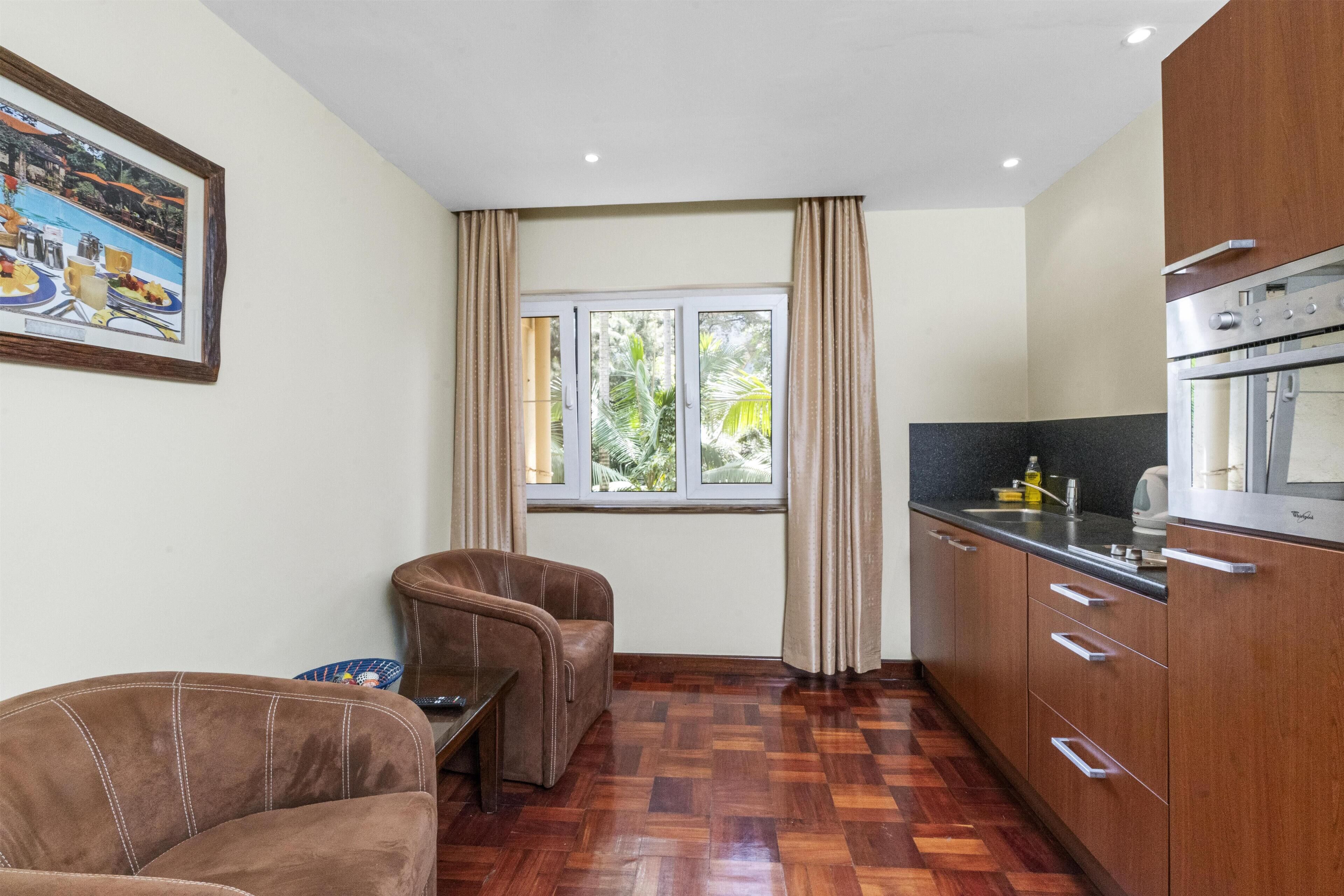 A compact kitchen with a dining area, wooden flooring, and a window with curtains.