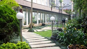 Un camino que conduce a un edificio con fachada de vidrio, rodeado de follaje y plantas en macetas.