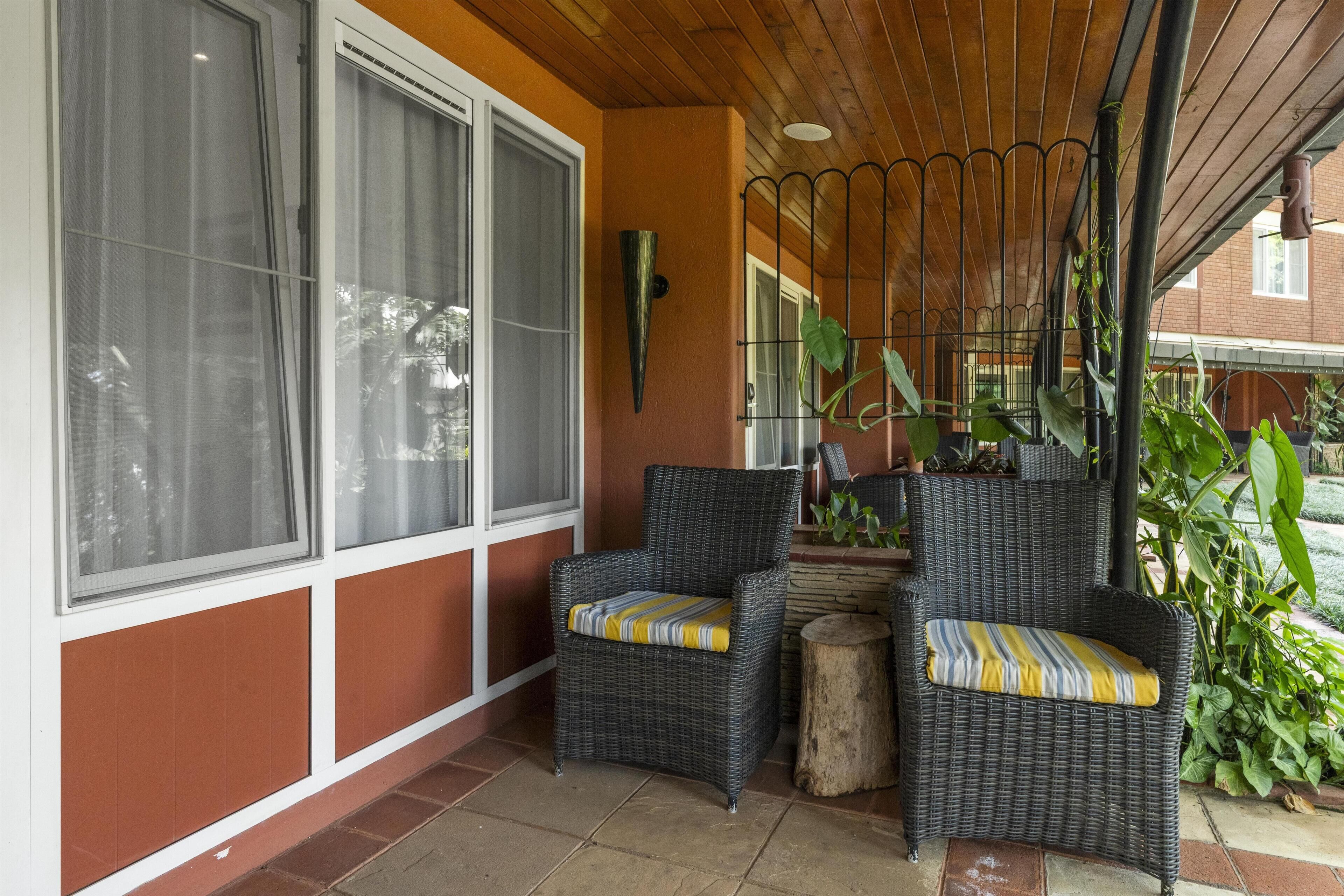 Een overdekt terras met rieten stoelen en een klein houten krukje.