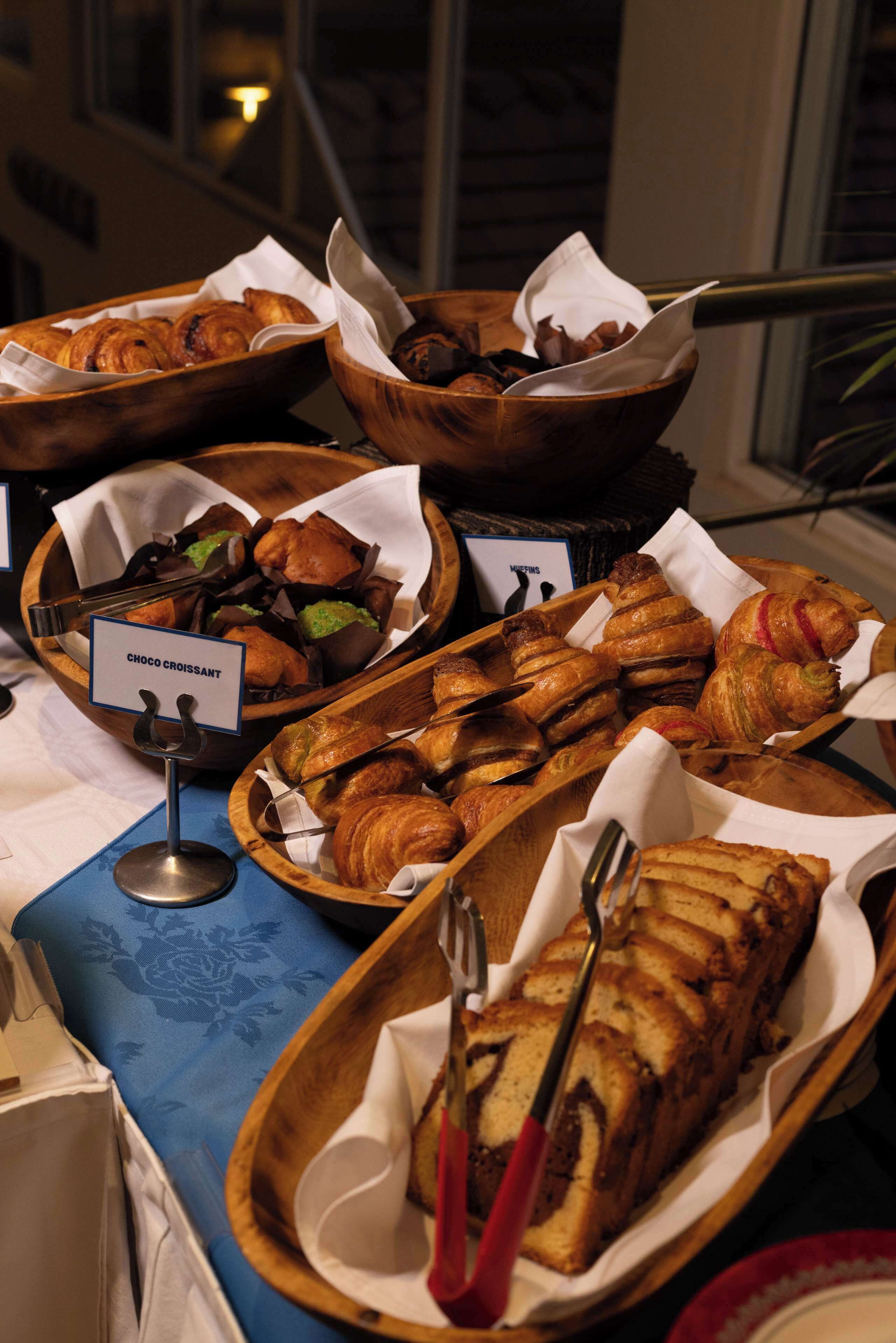 Una mesa de buffet con diversos productos horneados, como cruasanes y pasteles, dispuestos en cestas de madera.