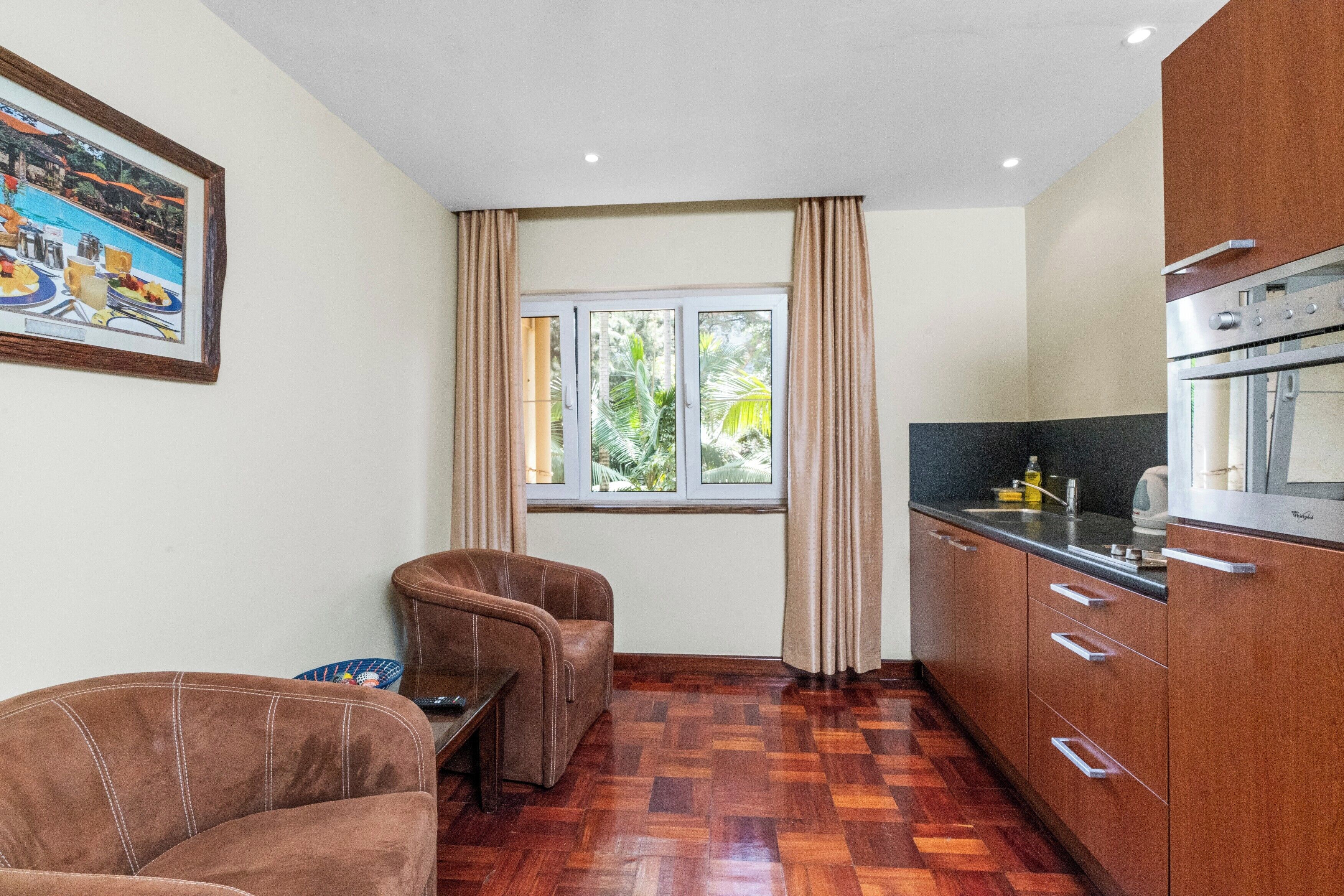 A compact kitchen with a dining area, wooden flooring, and a window with curtains.