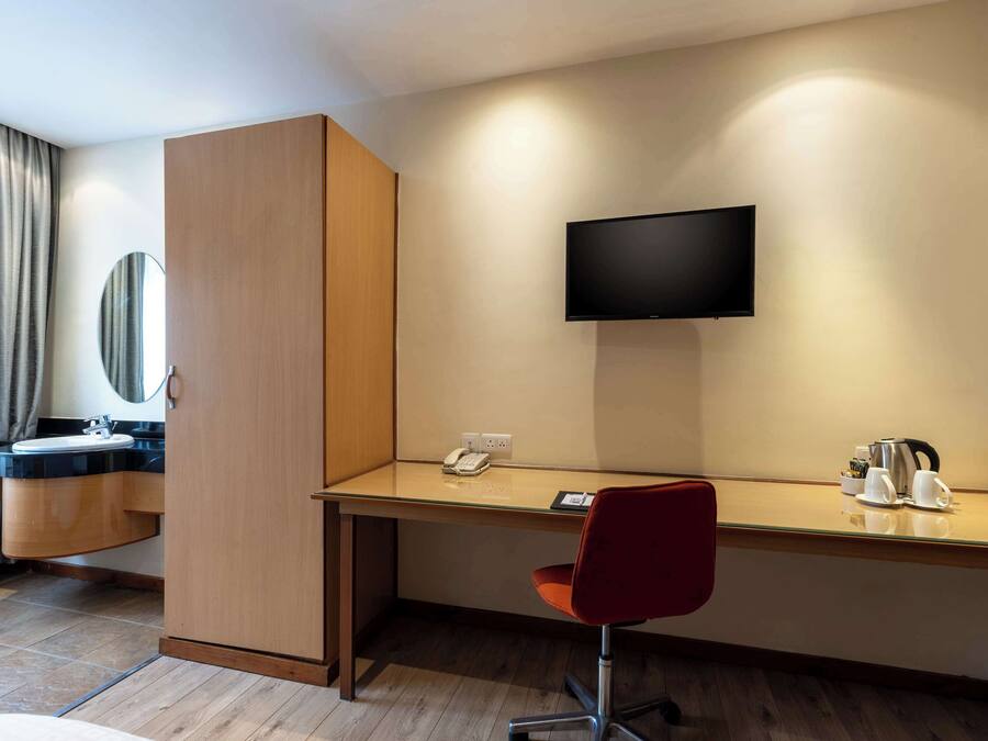 Habitación de hotel con un escritorio de madera, una silla roja, un televisor de pantalla plana montado en la pared, un teléfono y una cafetera.