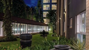 Un edificio moderno con fachada de vidrio, un jardín cuidado con una jardinera grande, y un cielo nocturno despejado.
