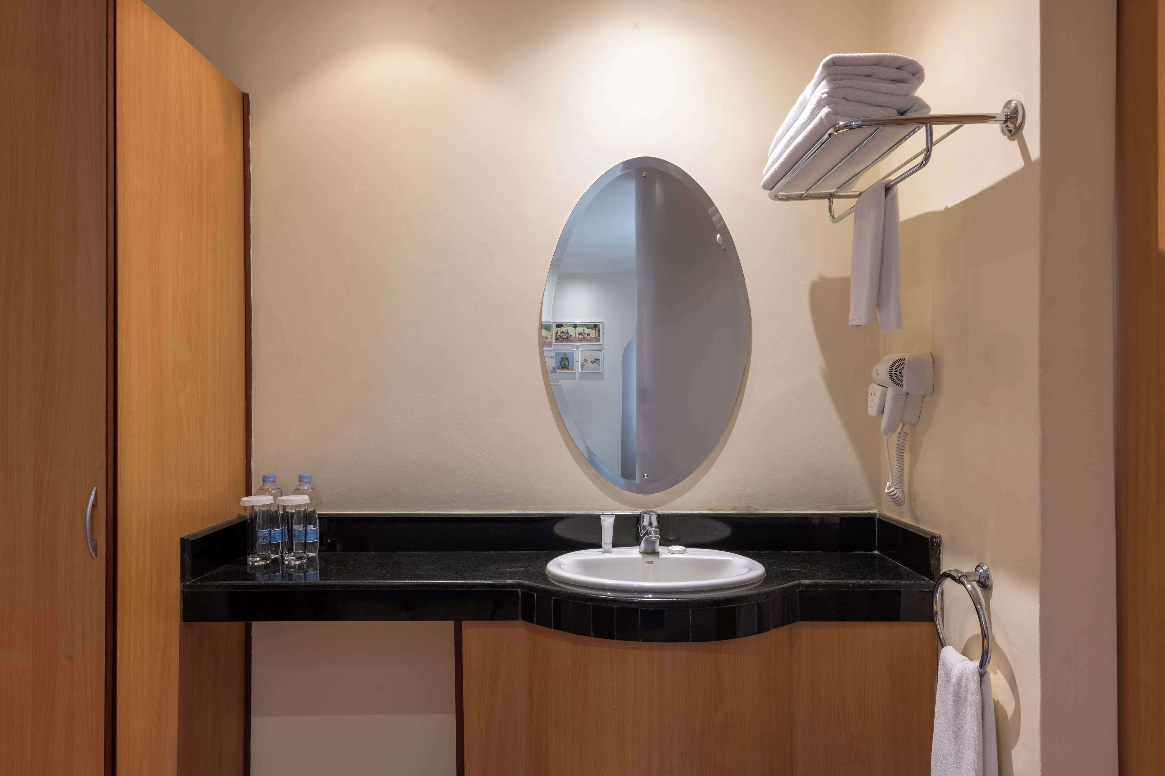 A bathroom with a black countertop, a white sink, a round mirror, a towel rack, and a phone.