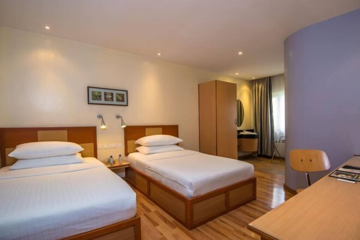 Habitación de hotel con dos camas, un escritorio, un armario y un espejo.